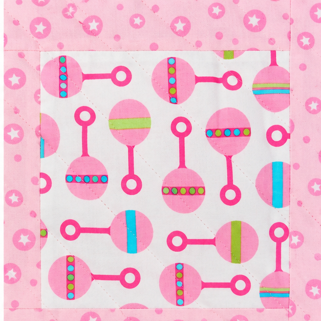 A close-up of a quilted fabric panel featuring a pink and white pattern of maracas with colorful stripes, surrounded by a pink border with white stars and dots.