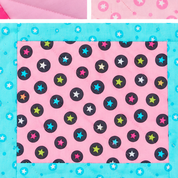 A close-up of a fabric or paper material swatch with a pink background, black circular dots, and scattered multicolored star motifs, bordered by a turquoise patterned edge.