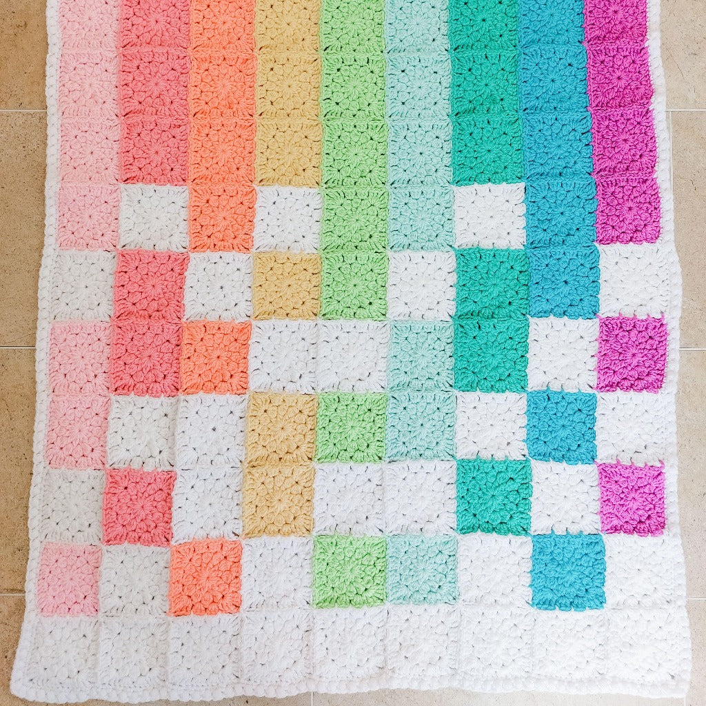 rainbow coloured flower squares on the baby blanket in colours of peach, pink, orange, yellow, green, aqua and purple.