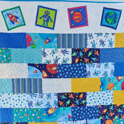 Children's quilt with space-themed fabric squares featuring rockets, robots, and planets.