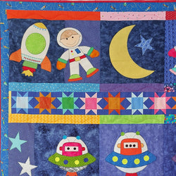 blue backgrounds showing a boy astronaut on an outer space quilt with a rocket, 2 alien spacecraft and a moon and stars