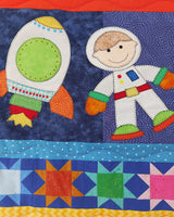 a rocket blasting into space next to a floating boy astronaut wearing a white space suit with brightly coloured patchwork stars underneath