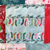 Patchwork fabric with Christmas-themed design of colorful socks on a branch.