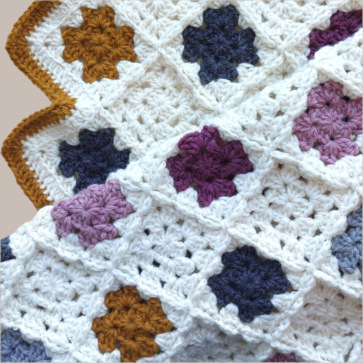 blanket folded over showing cream crochet granny squares alternating with pinks, greys and yellow