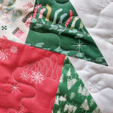 Close-up of a quilt with Christmas-themed fabric pieces including red mittens, green trees, and white snowflakes.