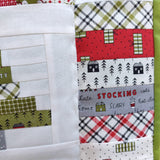 Close-up of a quilt with festive patterns including plaid, trees, and Christmas words such as stocking, scarf,cold