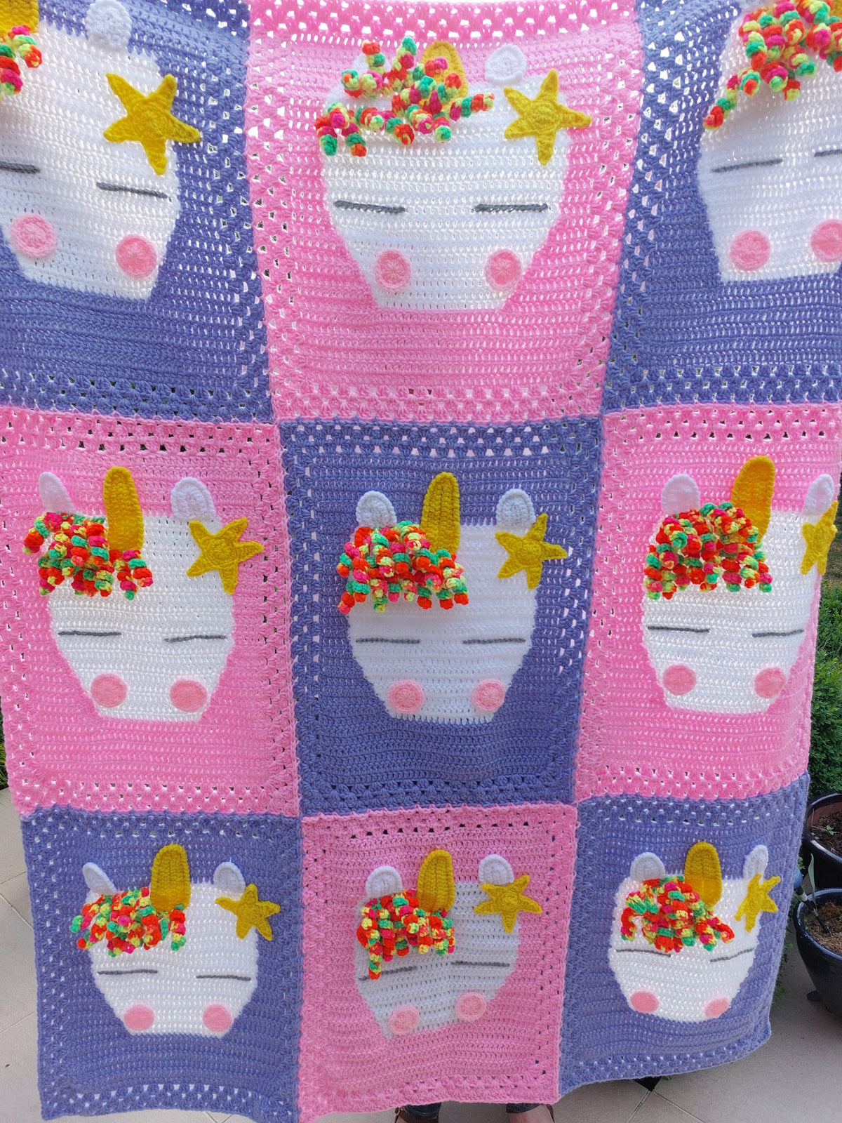 the whole of the handmade crochet unicorn blanket showing 5 purple sections crocheted together with 4 pink sections each one with a unicorn head on it