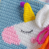 Close-up of a crocheted unicorn with a yellow horn and pink polka dots on a blue background.