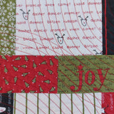 Close-up of a quilt with Christmas-themed patterns and text.