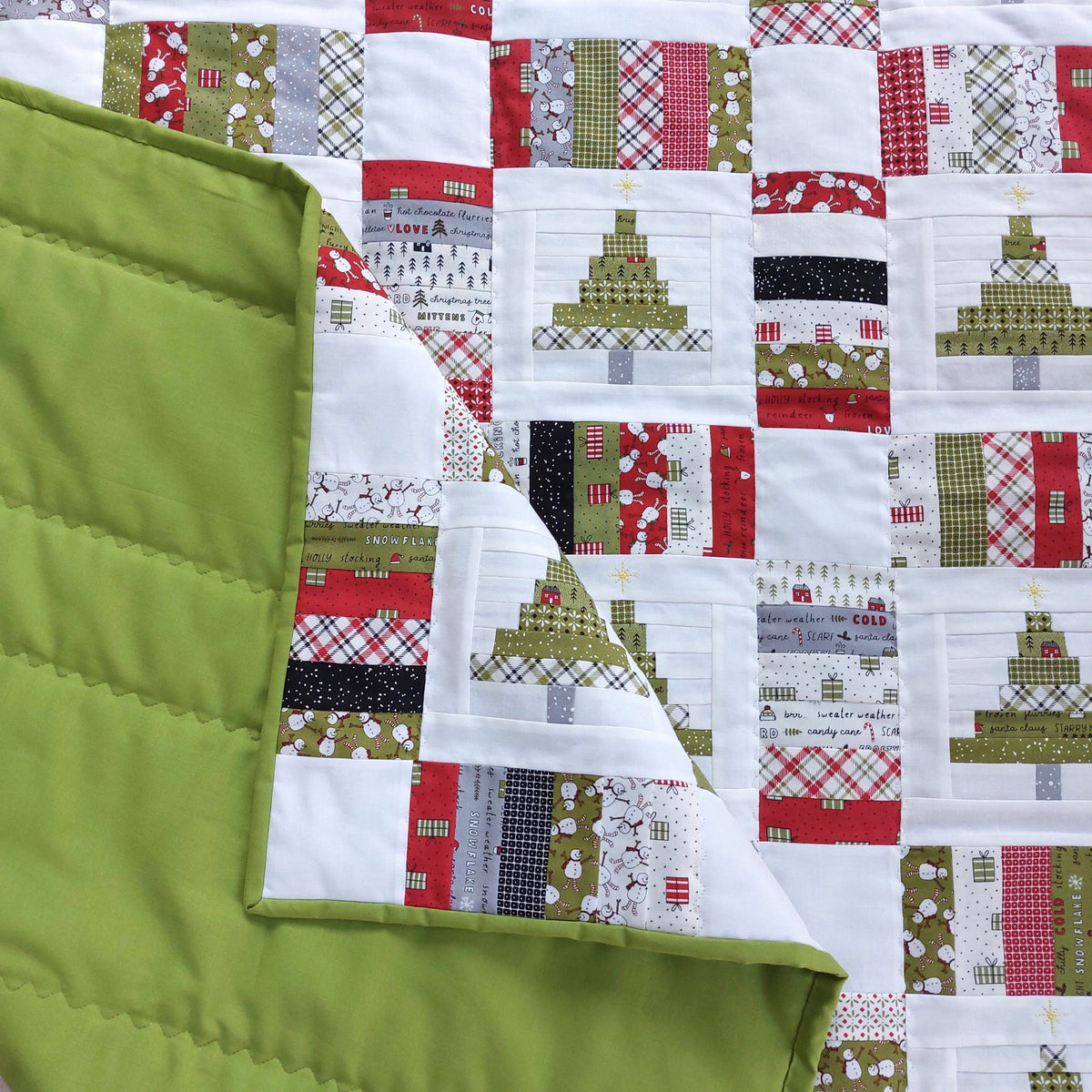A close-up of a handmade quilted blanket or quilt showing two sides: one side features a patchwork design of Christmas trees and holiday motifs in red, green, white, and black, while the other side is solid olive green with visible quilting stitches.