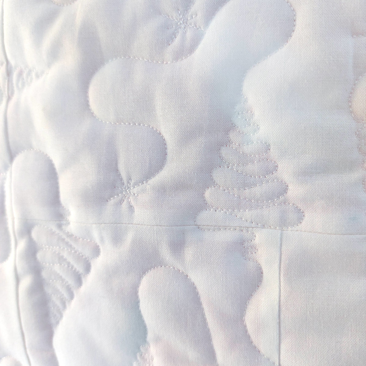 Close-up of a white quilted fabric with stitched cloud-like patterns and a tree motif.