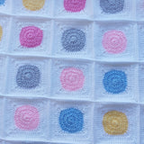 yellow, blue, grey and pink circles with white crochet around them to make squares joined together in this handmade crochet baby blanket