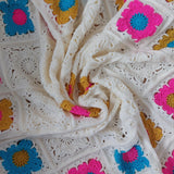 flower design granny squares in bright pink, gold, cream and blue. The blanket has been swirled around the centre