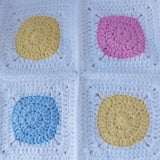 a baby blanket showing four crochet squares with pink, yellow and blue circles surrounded by white to make them square