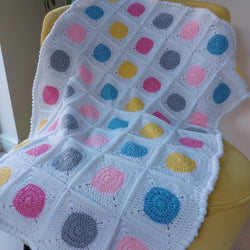 crochet baby blanket with pink, blue, grey and yellow circles surrounded in white to make squares