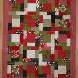 An overhead view of a Christmas quilt with squares and rectangles in reds, greens, black and white colours