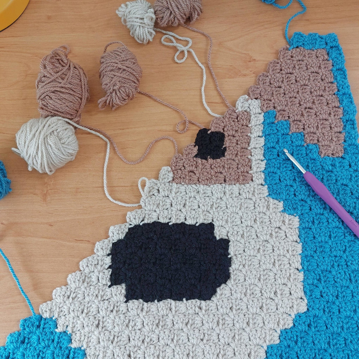 photo of the cute puppy baby blanket in production with balls of wool and a crochet hook