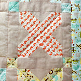 a photo of the crosses quilt showing one of the crosses made up of patches in  a white fabric with orange elephants