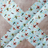 close up photo of the patchwork cross, the fabric of the cross is blue with red, blue and green aeroplanes