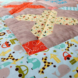 a close up photo of the baby quilt showing blue border fabric with elephants, cars, whales and giraffes printed on it. There is a yellow cross made up of patchwork squares