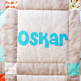 a close up photo of the name Oskar in blue fabric which had been sewn to the front of the quilt