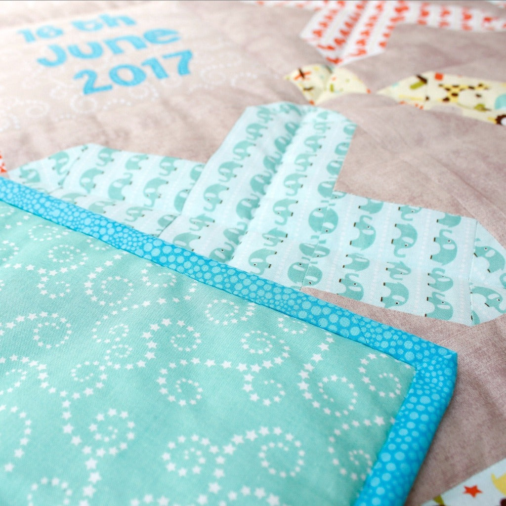 close up photo of the front of the quilt showing patchwork cross made from blue elephant fabric and the back of the quilt of aqua fabric with swirls of stars