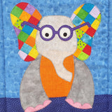a blue background with a grey elephant who has an orange body, pink toes , purple glasses and ears that are made from 1 inch square fabric pieces