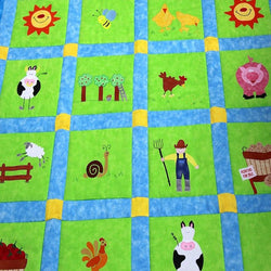 Large green patchwork squares surrounded by a blue and yellow border. On each of the squares is a sun, cow, sheep, farm boy and pig