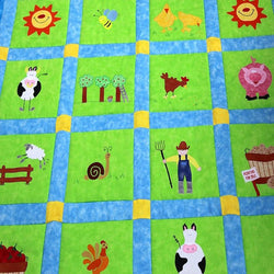 Large green patchwork squares surrounded by a blue and yellow border. On each of the squares is a sun, cow, sheep, farm boy and pig