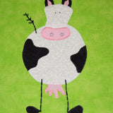 a bright green fabric background with a black and white cow with pink udders
