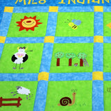 Large green patchwork squares surrounded by a blue and yellow border. On each of the squares is a sun, cow, sheep, farm boy and pig