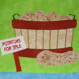 bright green fabric background with a wooded barrel pf potatoes with a sign saying potatoes for sale