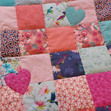 patchwork squares of pink, orange and blue squares. some squares have brightly coloured hummingbirds on them and others have flowers, there are also two hearts in pink and blue
