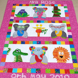 A quilt with a pink border showing 4 elephants, a hippo, giraffe, lion, a smiling crocodile and a lion
