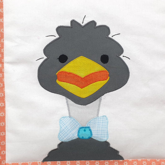 a white fabric background with a grey smiling emu wearing a blue bow tie on the land down under quilt
