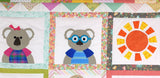 a portion of the land down under quilt showing a girl koala in a purple dress with a pink bow on her head and a male koala with a blue t shirt and blue glasses