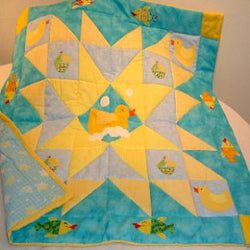 a patchwork quilt using triangles in aqua and yellow with a duck in the centre having a bath with fish and boats around the outside
