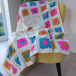 bright granny square blanket with squares of bright blue, pink and gold
