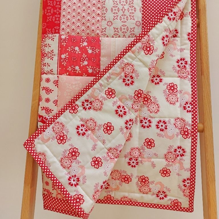 patchwork quilt with patches of different flowers in shades of pink and red and showing the back fabric of flowers