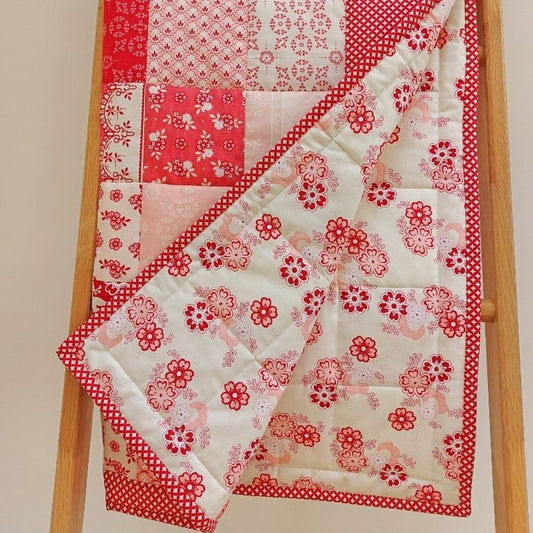 patchwork quilt with patches of different flowers in shades of pink and red and showing the back fabric of flowers