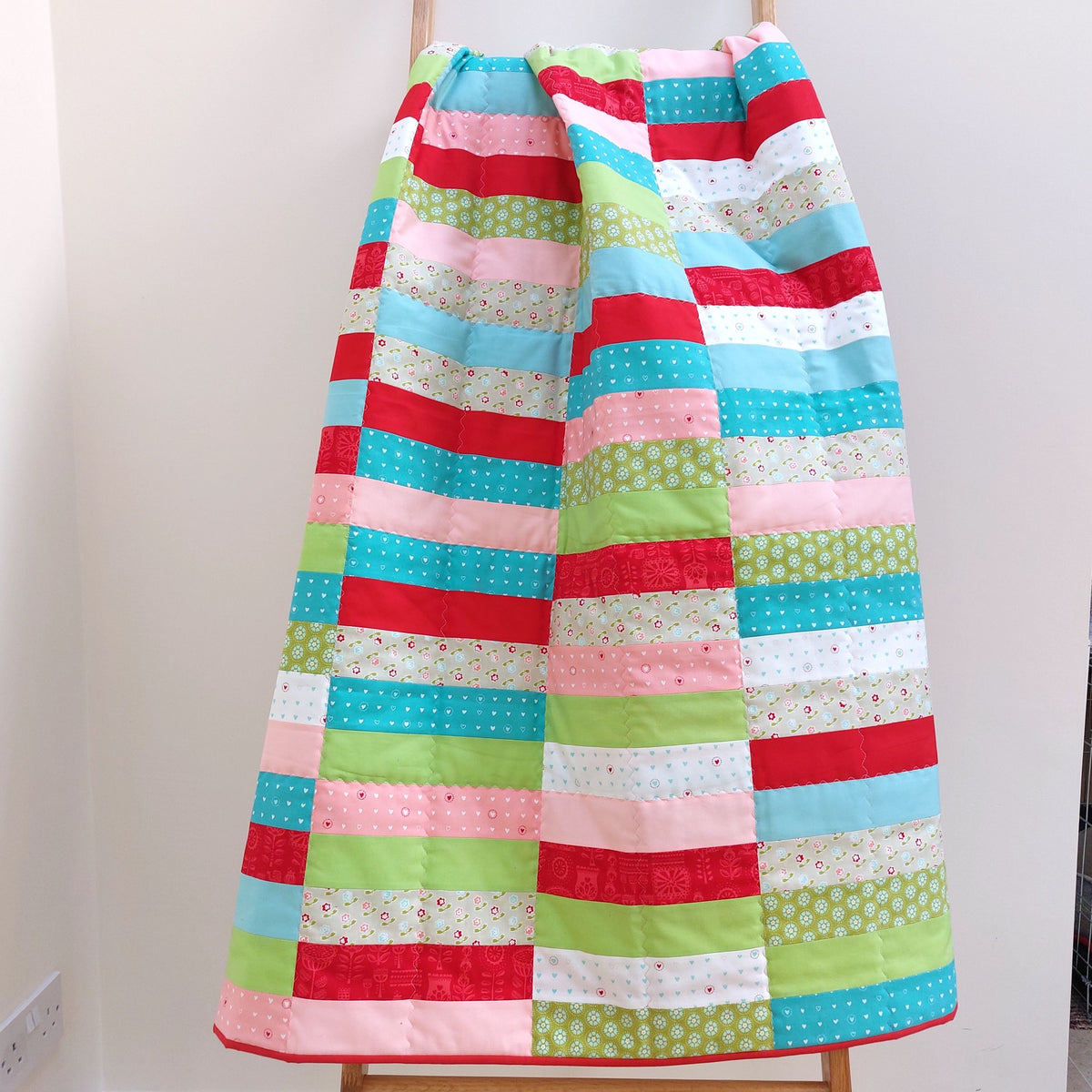 the coin quilt draped on a quilt ladder
