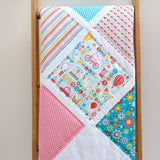 the patchwork quilt of big squares showing flowers, cameras, sweet machines and butterflies all on a quilt folded over a quilt ladder