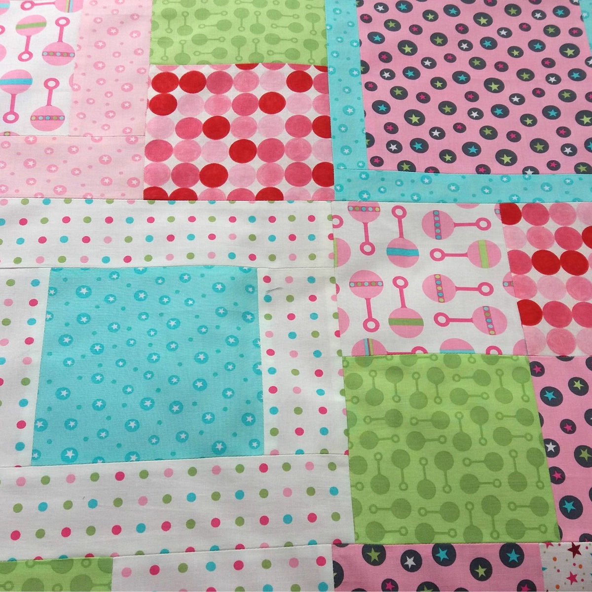 A multicolored baby quilt with patches featuring rattles, stars, and hearts on a white background.