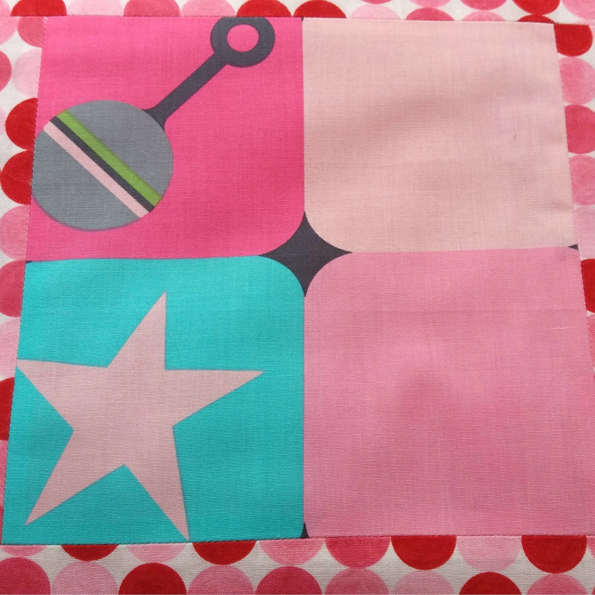a close-up of the fabric which shows squares of pink and blue with a printed rattle and a star