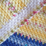 the border of the baby blanket in white with s yellow edge laid on top of the blanket which has yellow and then blue stripes