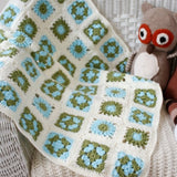 a cream, blue and green crochet baby blanket. Each crochet square is a flower of blue, cream and green