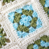 A close up picture of one of the granny squares in the handmade crochet baby blanket. The square is in blue and green with a cream edge.
