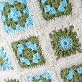 A close up of the granny squares which make up this baby blanket. The squares are in a flower motif in blue and green with a cream edge.