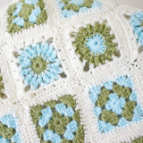 close up of the granny squares in a handmade crochet baby blanket. The squares are of a flower motif in the. colours of blue, green and cream