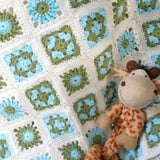 a handmade crochet baby blanket of flower squares in cream, green and blue